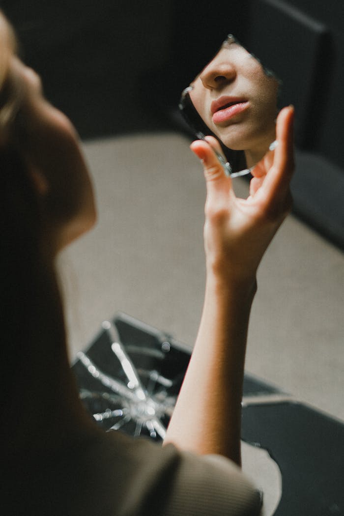 Close-up of a teenage girl holding a broken mirror, her lips reflected indoors.